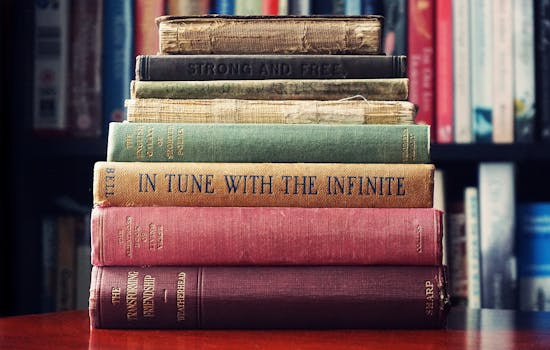 A stack of vintage hardcover books on a wooden table in a cozy library setting.